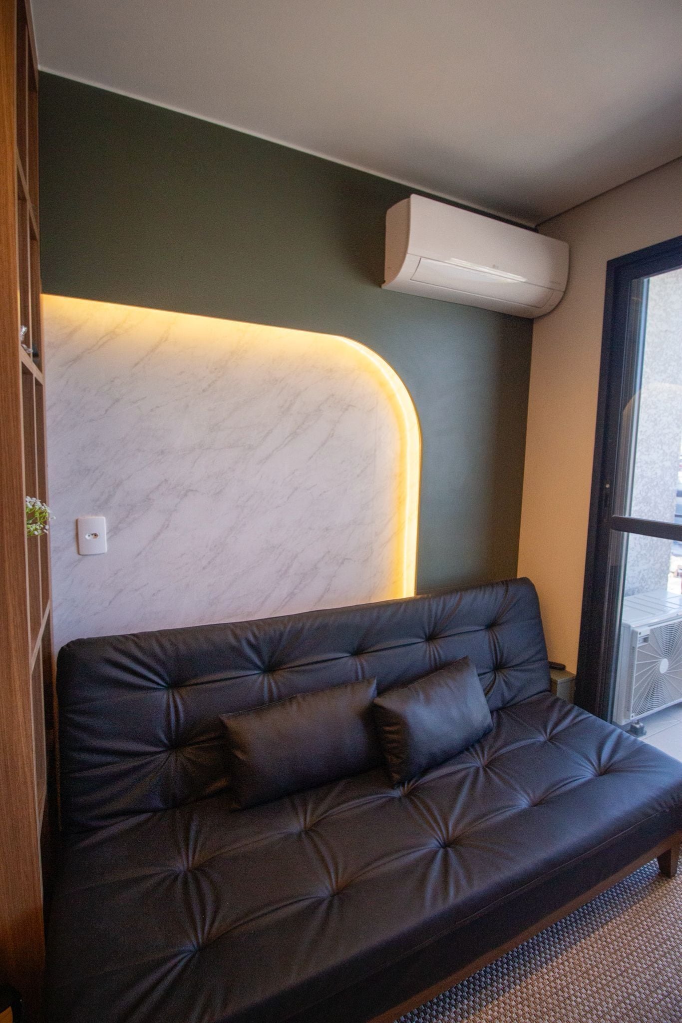 A modern interior with a dark leather sofa, a marble accent wall, and a large window.