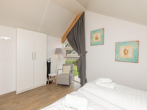 A bedroom with a bed, a chair, a desk, and a window with curtains. - Beachside Modern Holiday Home for 6 (Renesse)