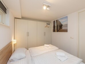Une chambre d’hôtel avec deux lits, une armoire, un tableau au mur et un porte-manteau suspendu.