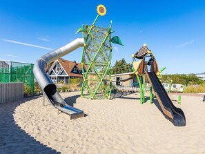 A playground with slides and climbing structures, surrounded by a sandy area and buildings in the background. - Beachside Modern Holiday Home for 6 (Renesse)