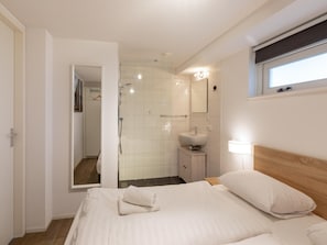 Une chambre d’hôtel avec un lit, une salle de bain avec une douche, un lavabo et un miroir.
