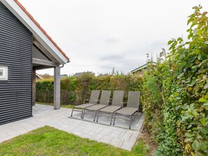 A patio area with a covered seating arrangement and a view of a residential property. - Beachside Modern Holiday Home for 6 (Renesse)