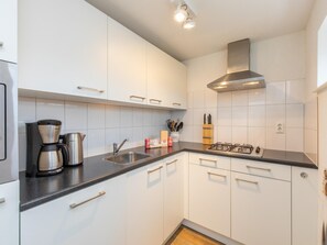 Eine moderne Küche mit weißen Schränken, einem Gasherd, einer Kaffeemaschine und einem Spülbecken.