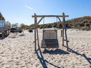 Une balançoire en bois installée sur une plage de sable, avec une dune en arrière-plan.