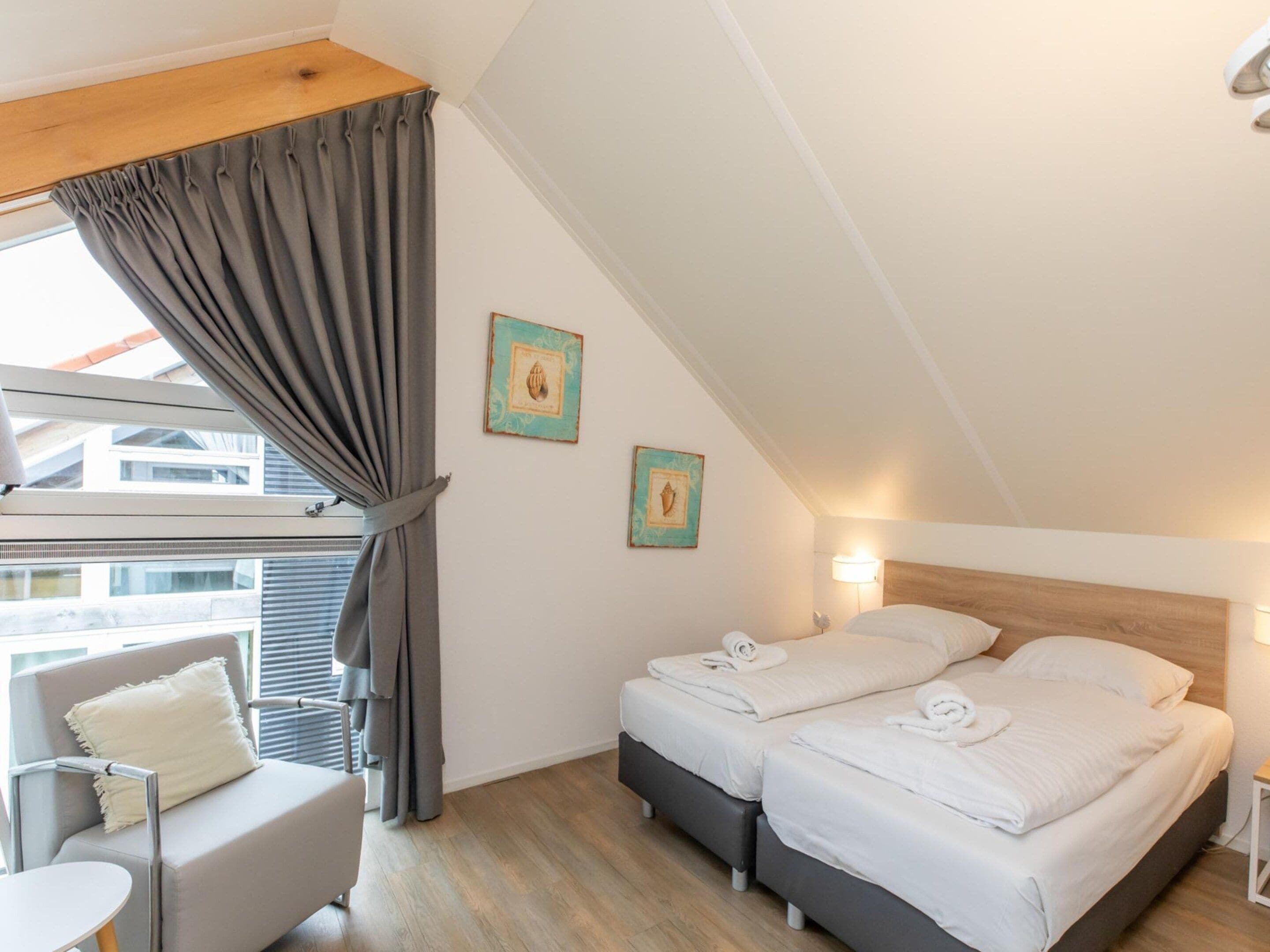 Una camera d'albergo con due letti, un tavolino, una sedia e una finestra con tende.