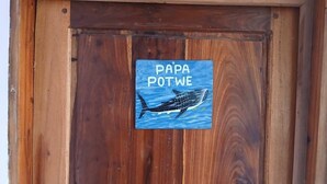A wooden door with a sign that reads "PAPA POTWE" and an illustration of a whale. - Magogoni Guest House (Mafia Island)