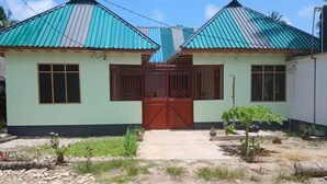 A two-story house with a red gate, a small garden, and a dirt driveway. - Magogoni Guest House (Mafia Island)