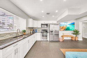 A modern kitchen with white cabinets, stainless steel appliances, and a large island with a sink.
