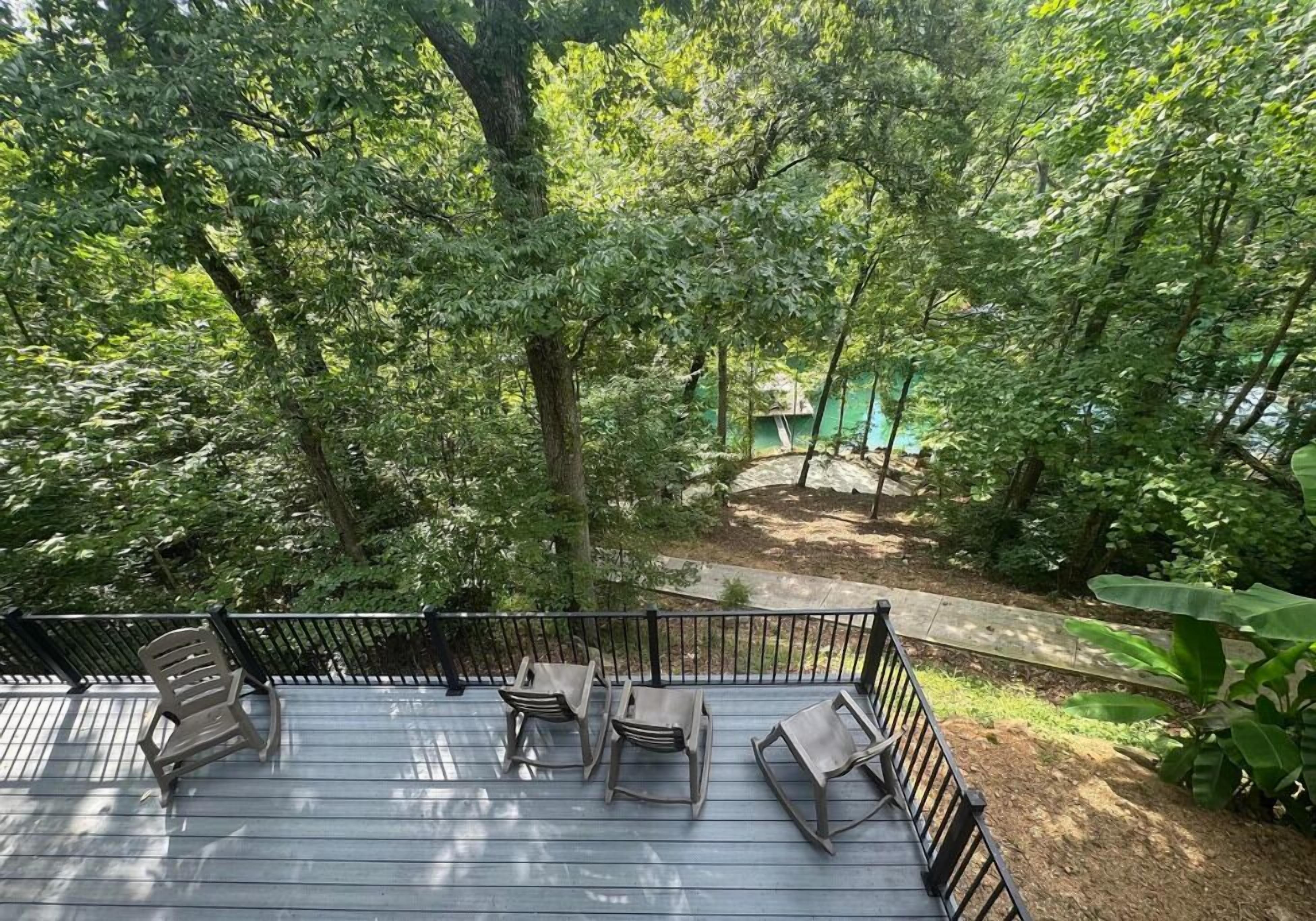 A wooden deck with four chairs and a table, surrounded by dense greenery and trees.