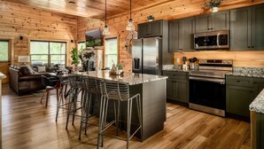A wooden cabin interior with a kitchen featuring stainless steel appliances, a bar area, and a living room with a sofa and coffee table. - Free Dollywood Tix•Heated Pool•GameRoom•Modern (Sevier)