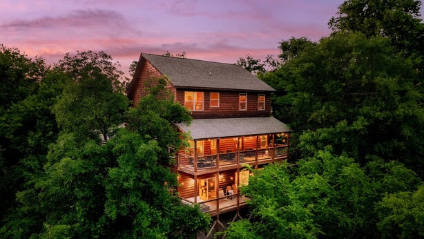A multi-story log cabin with a balcony, surrounded by dense trees. - Free Dollywood Tix•Heated Pool•GameRoom•Modern (Sevier)