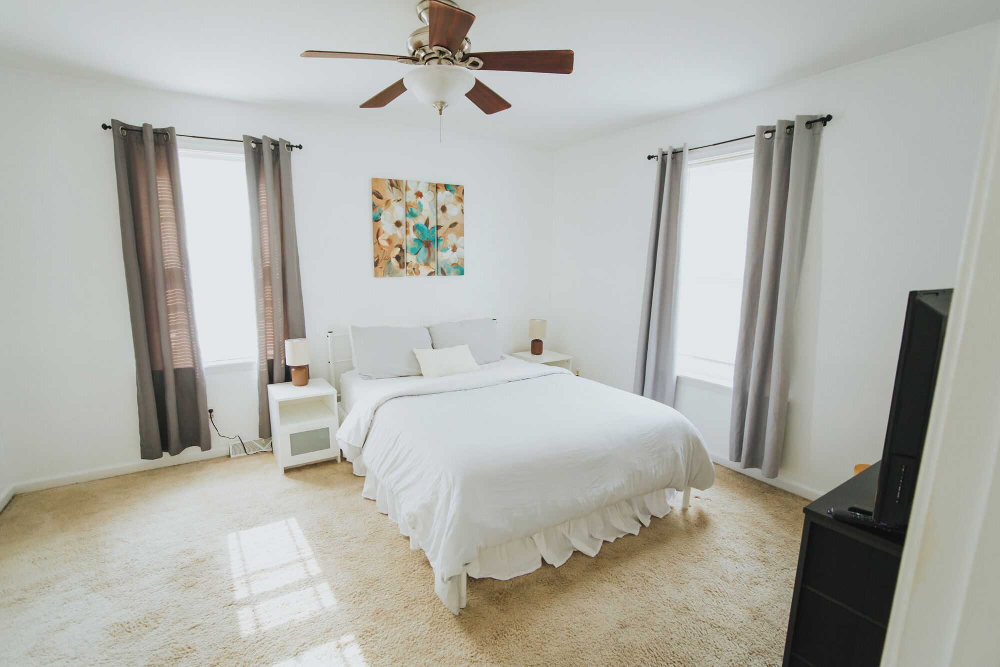 Une chambre à coucher avec un lit, des tables de chevet, un ventilateur de plafond et un tableau accroché au mur.