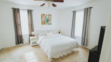 Une chambre à coucher avec un lit, des tables de chevet, un ventilateur de plafond et un tableau accroché au mur.