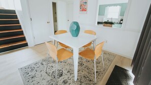 Een eetgedeelte met een witte tafel, oranje stoelen en een turquoise vaas.