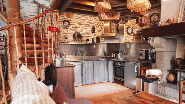 Eine rustikale Küche mit einer Holztreppe, Steinwänden und einem Holztisch.