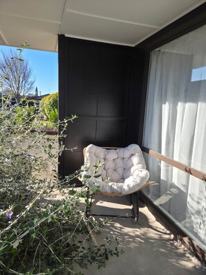 Un rincón de una habitación con una butaca blanca acolchada, una pared oscura y un ventanal con cortinas de encaje.