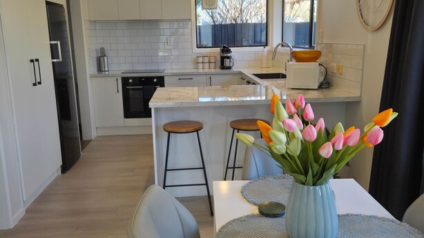 Una cocina moderna con armarios blancos, una isla central y una zona de comedor con un jarrón de tulipanes.