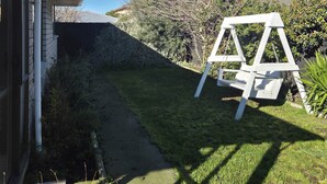 Una propiedad residencial con cielo despejado, jardín cubierto de césped, un columpio blanco y una casa con canalones visibles.