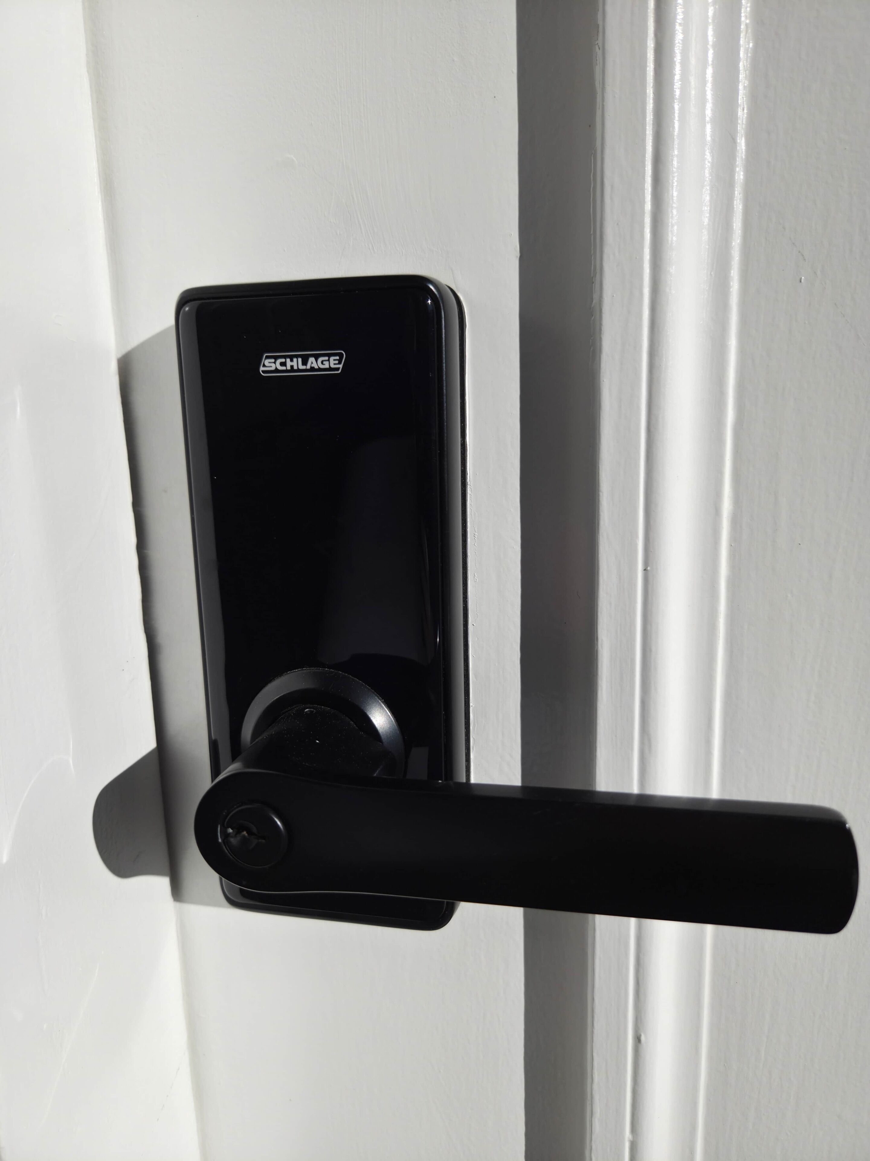 Une poignée de porte SCHLAGE noire sur une porte blanche.