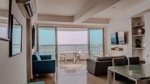 Ein modernes Wohnzimmer mit Glastür zu einem Balkon, einem Essbereich und einem an der Wand befestigten Fernseher.