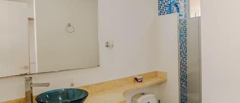 A bathroom with a blue glass basin, a white toilet, and a shower area with blue tiles.