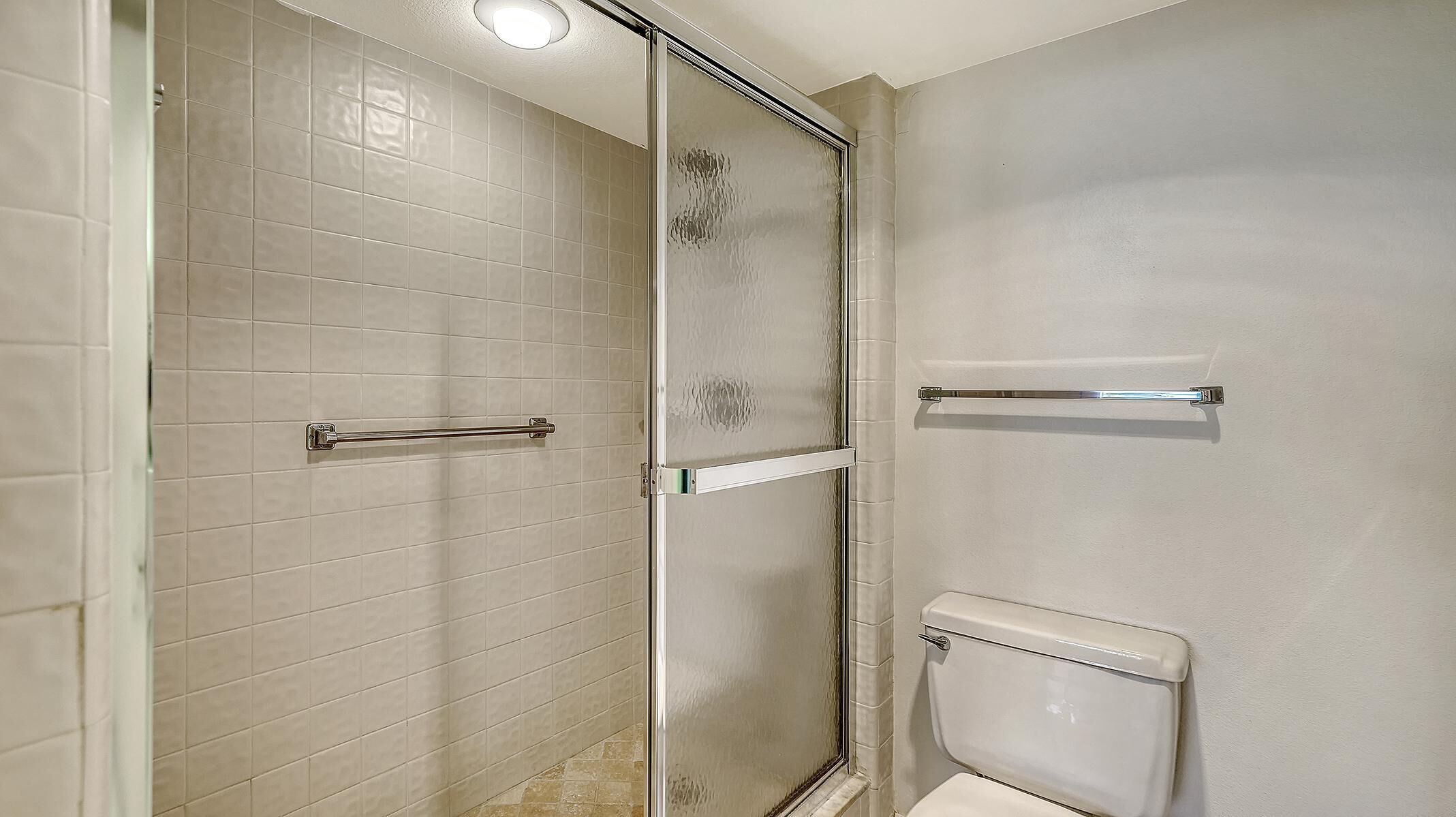 A bathroom with a glass shower enclosure, a white toilet, and a towel rack.