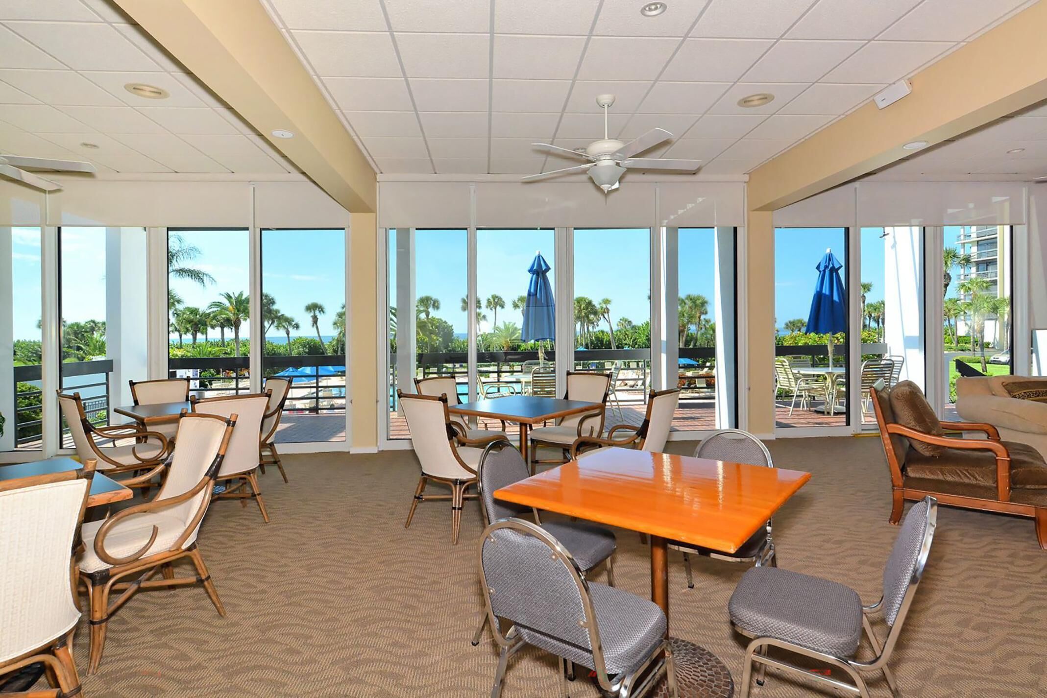 A spacious indoor area with large windows, a ceiling fan, and various seating arrangements including tables and chairs.