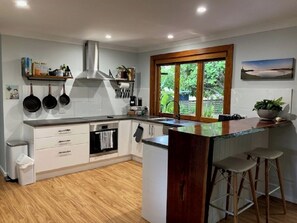 Een moderne keuken met witte kastjes, een roestvrijstalen afzuigkap, een houten aanrechtblad en een raam met uitzicht op groen.