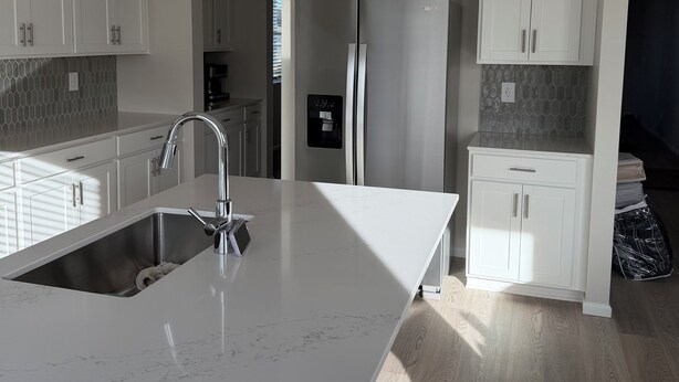 Una cocina moderna con armarios blancos, un refrigerador de acero inoxidable y una encimera de mármol.