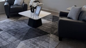 Una sala de estar moderna con dos sofás de cuero negro, una mesa de centro blanca y una alfombra estampada.