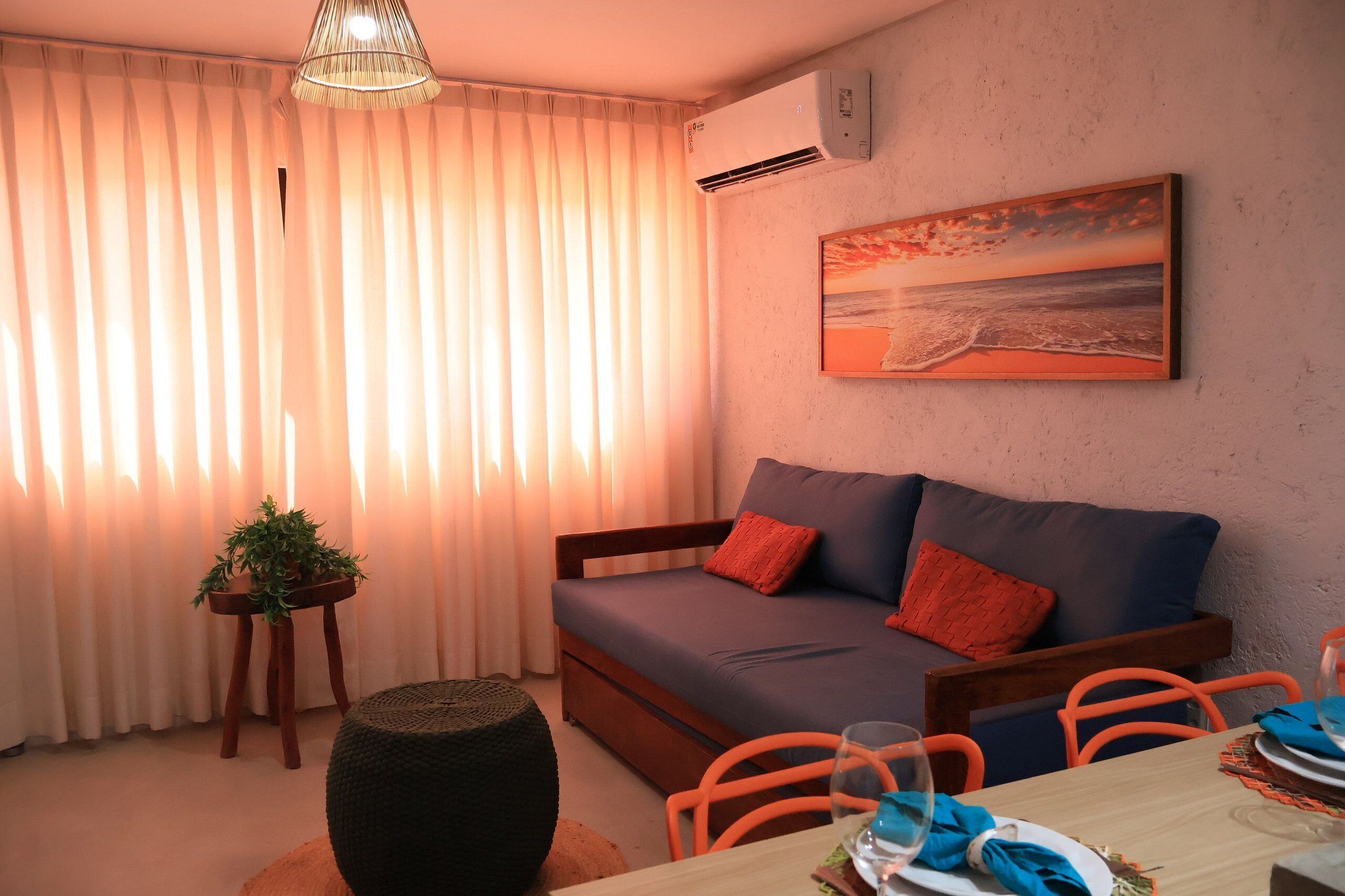 A cozy room with a sofa, a dining table, a potted plant, and a painting on the wall.