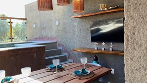 Ein Holzespeisesaal mit Stühlen, ein an der Wand befestigter Fernseher und Korbstuhl-Pendelleuchten.