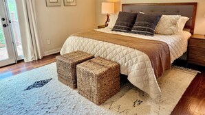 Une chambre à coucher avec un grand lit, une table de chevet, une lampe, deux tableaux encadrés au mur et une porte-fenêtre coulissante.