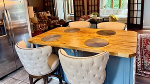 Une cuisine avec un îlot central en bois, des chaises à assise rembourrée de couleur blanche et un réfrigérateur en acier inoxydable.