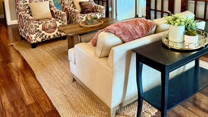 Un salon chaleureux avec un plafond en bois, un canapé à motifs, un divan blanc et une table basse de couleur sombre.