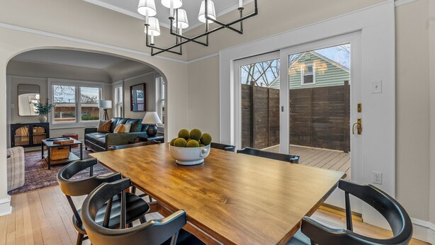 A spacious dining area with a wooden table and modern chairs, a chandelier, and a view of the backyard through large sliding glass doors.