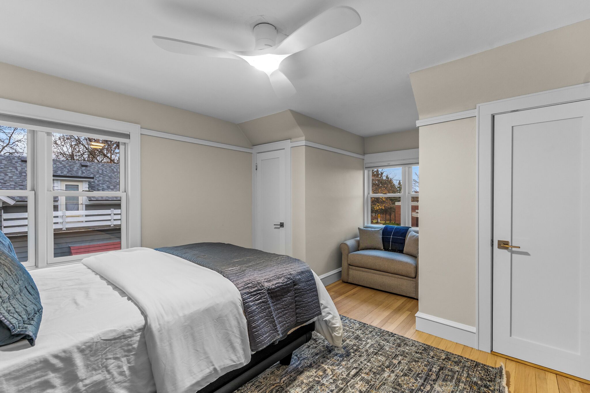 A bedroom with a bed, a ceiling fan, a sliding glass door, a sofa, and a wardrobe.