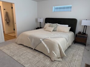 A bedroom with a large bed, two bedside tables with lamps, a window with blinds, and a door leading to another room. - Midtown Heights Townhome: EV Charger & walkable to BSU Campus. (Boise)