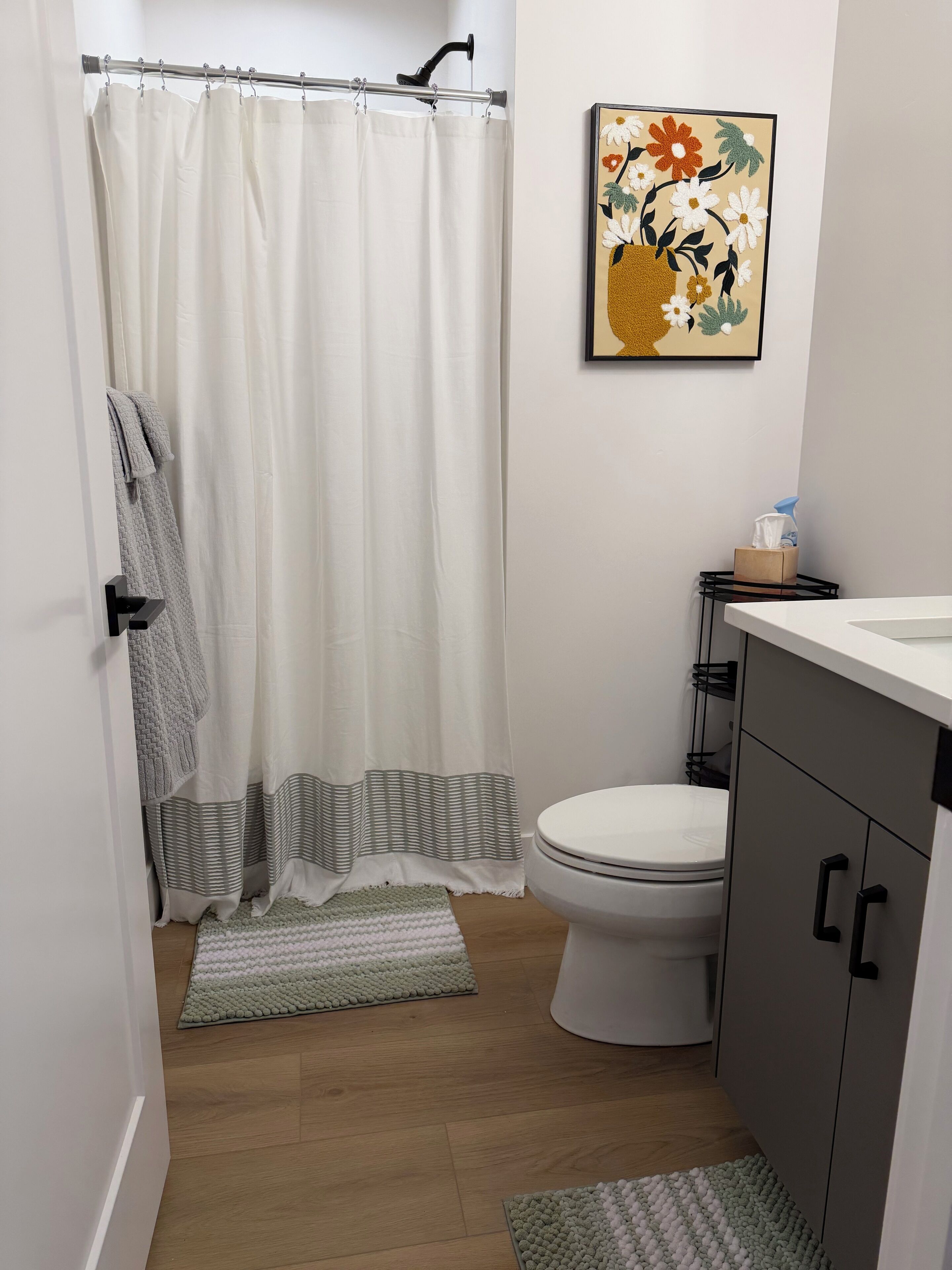 Een badkamer met douchegordijn, toilet, wastafel, een bloemig kunstwerk in een lijst en een handdoekrek.
