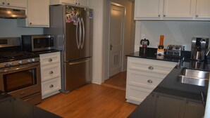 A modern kitchen with stainless steel appliances, white cabinetry, and a wooden floor. - 3-bedroom Cottage new LSU! (Baton Rouge)