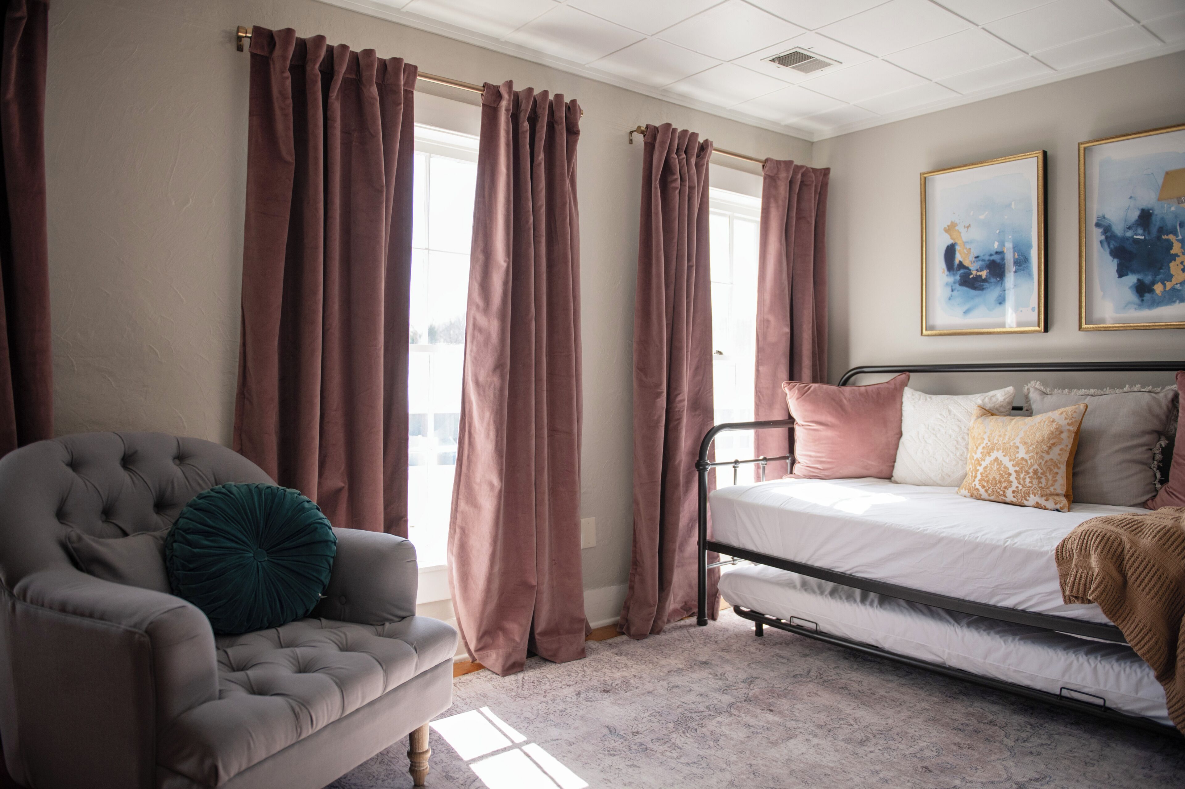 A bedroom with a bed, a chair, curtains, and two framed artworks on the wall.