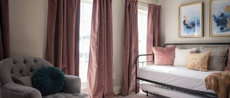 A bedroom with a bed, a chair, curtains, and two framed artworks on the wall.