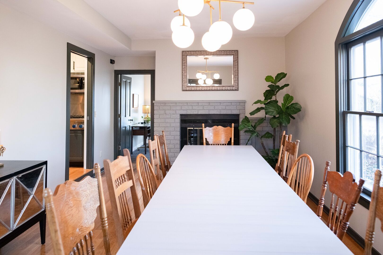 Un espace repas avec une longue table, des chaises en bois, une cheminée et une grande fenêtre.