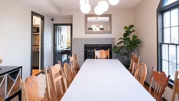 Un espace repas avec une longue table, des chaises en bois, une cheminée et une grande fenêtre.