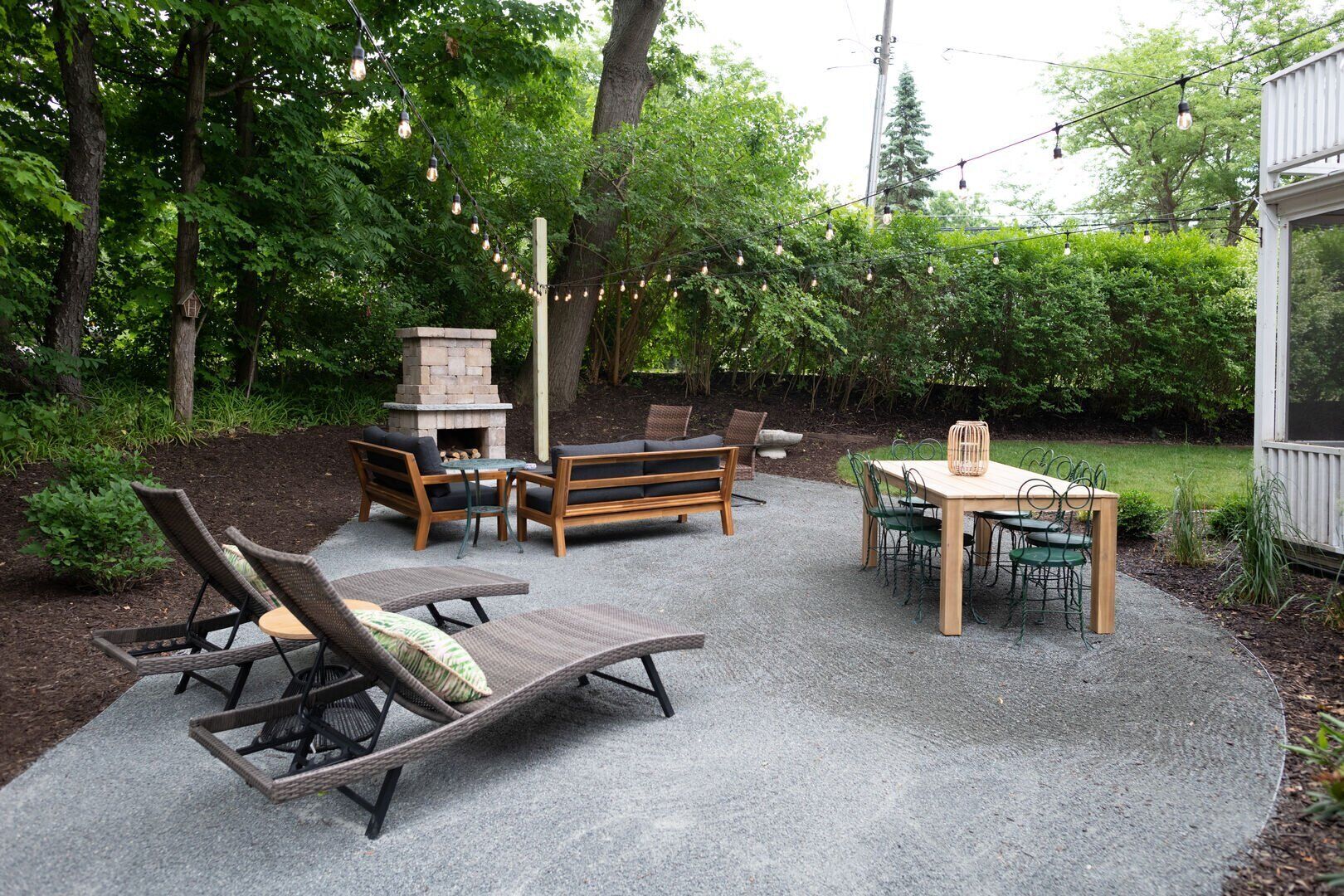 Un patio al aire libre con un hogar de piedra, mobiliario de madera y luces colgantes.