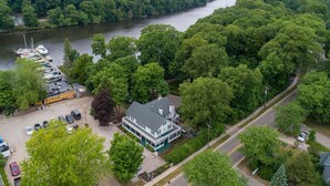 Een pand aan de rivier met een groot huis, een steiger met boten en een parkeerplaats.