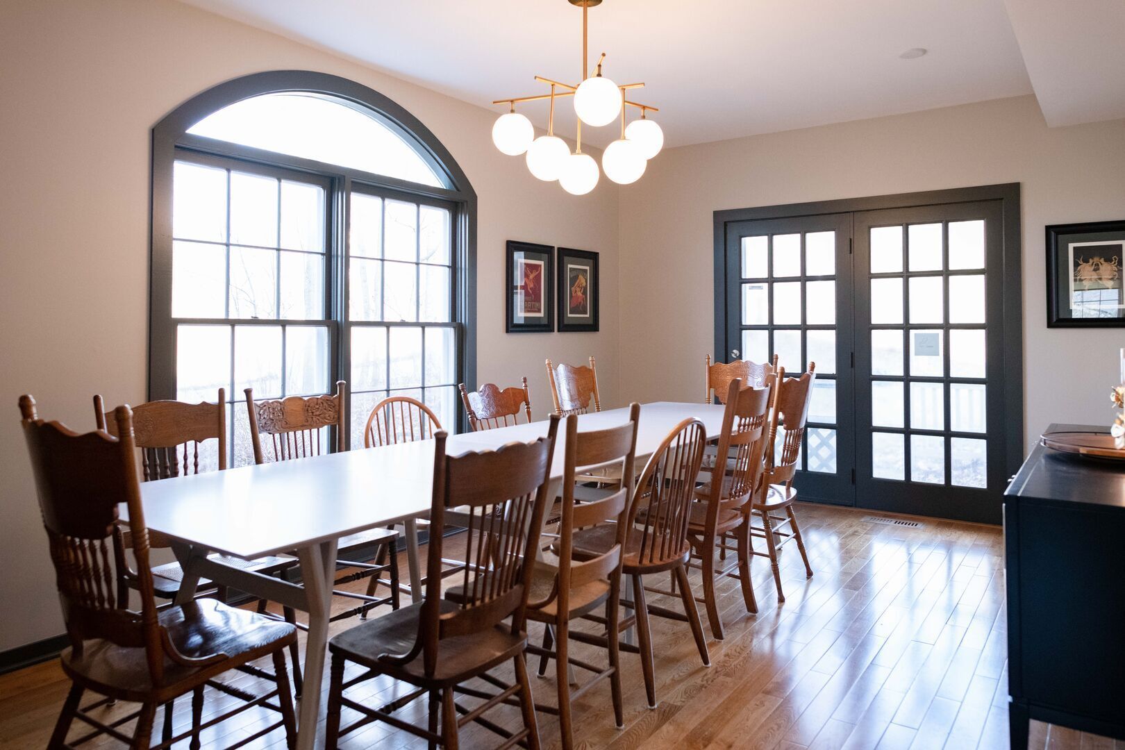 A dining area with a long table and multiple chairs, large windows, and a chandelier.