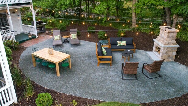 Een terras buiten met een houten tafel en stoelen, een zithoek en een stenen open haard.