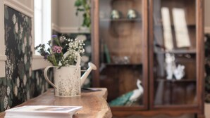 A wooden table with a white mug and a book, a wooden cabinet with glass doors, and a framed picture on the wall.