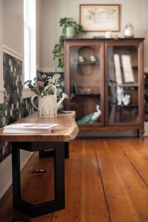 Una mesa de madera con una taza blanca y un libro, un aparador de madera con puertas de cristal, y un cuadro en la pared.